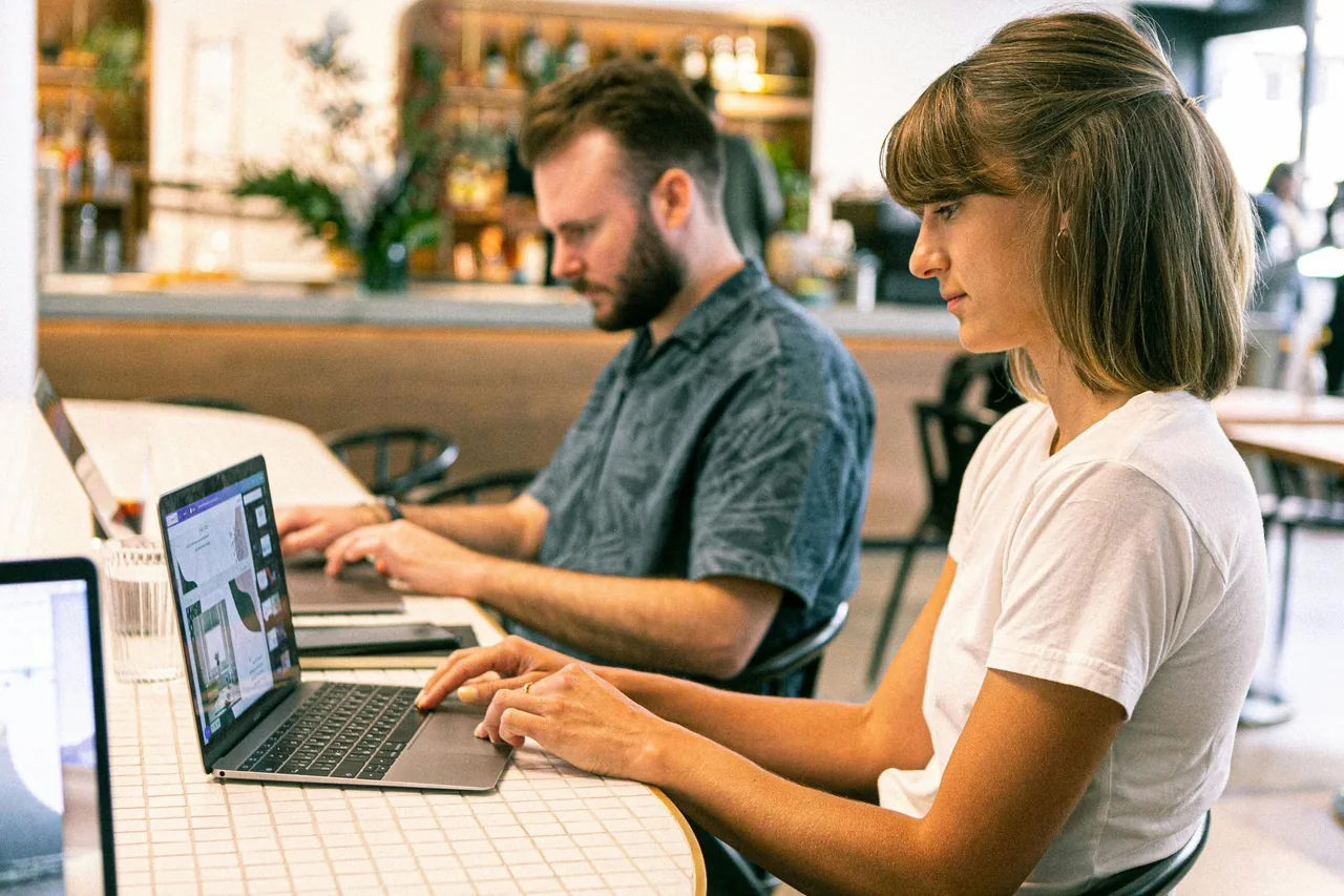 Two people working on laptops at a shared table.