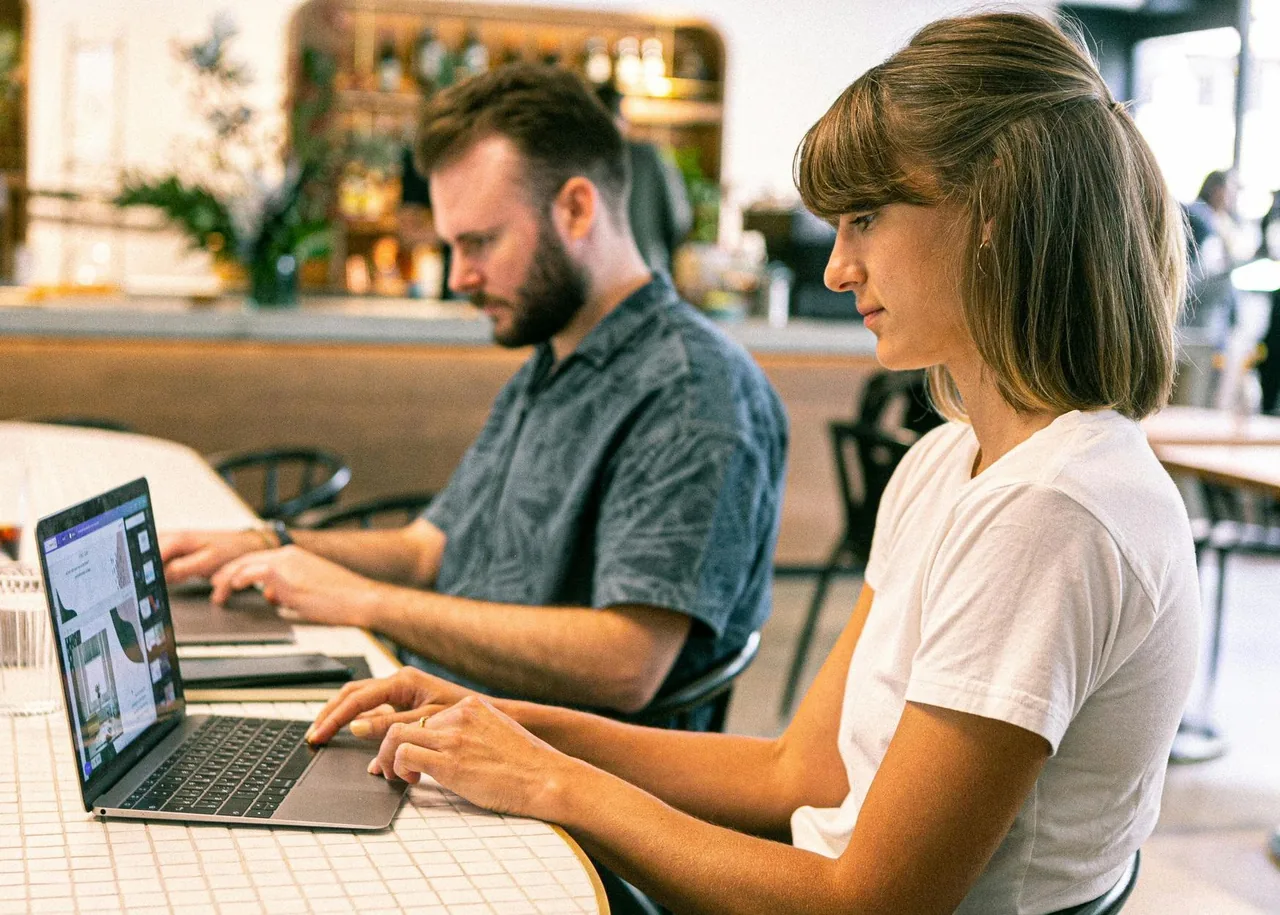 Two people working on laptops at a shared table.