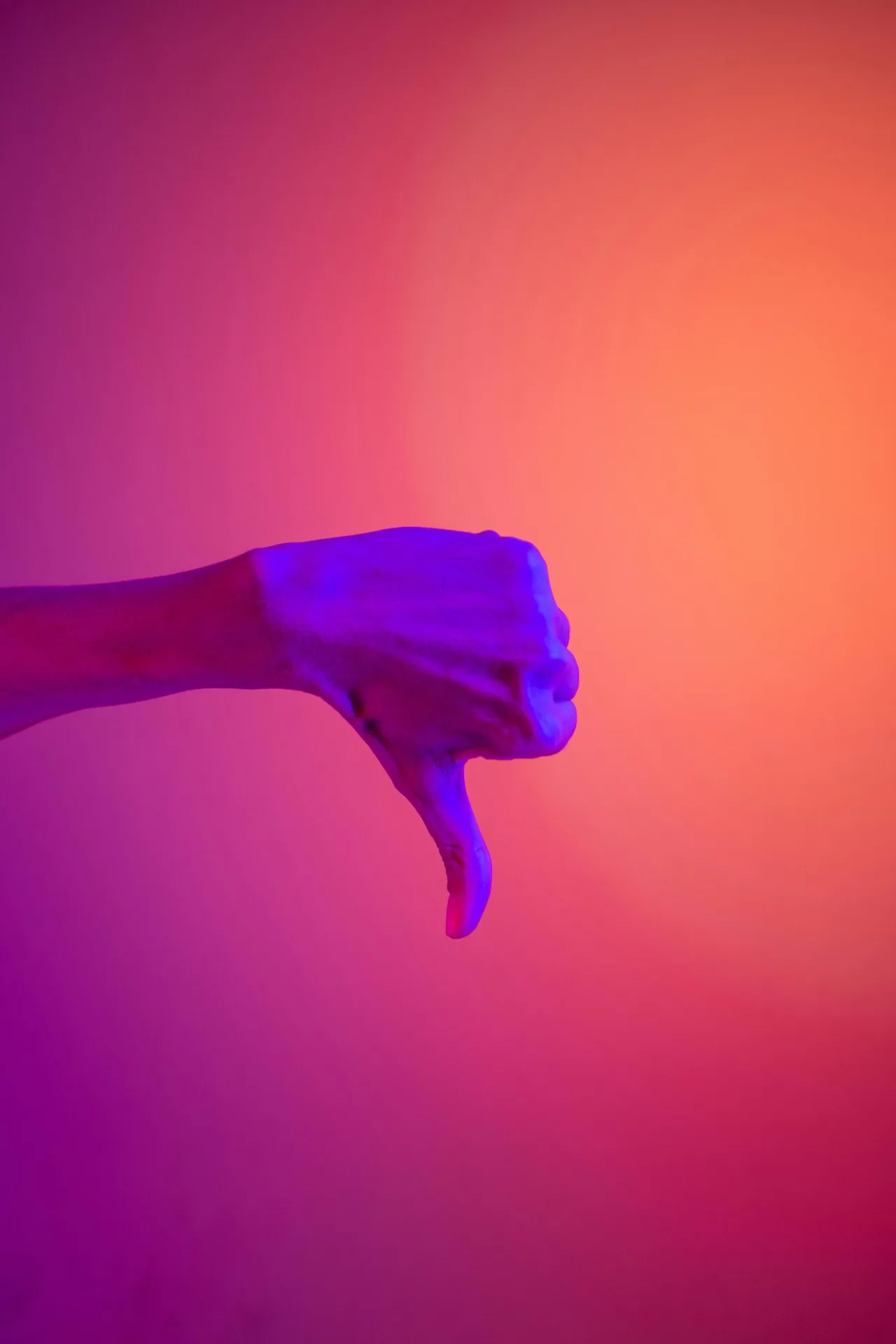 Hand giving a thumbs-down gesture against a coloured background.
